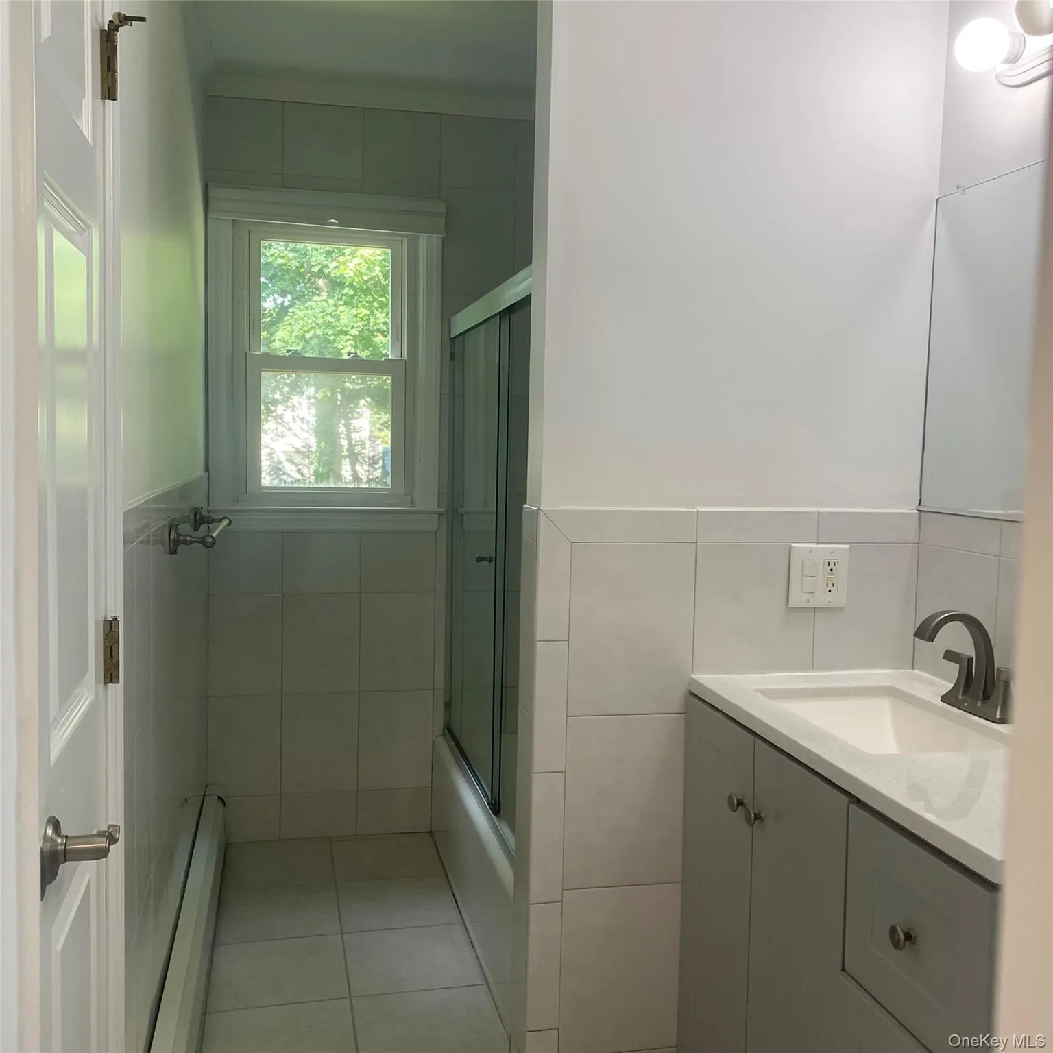 Full bath with a baseboard radiator, tile walls, vanity, tile patterned floors, and enclosed tub / shower combo Full bath with a baseboard radiator, tile walls, vanity, tile patterned floors, and enclosed tub / shower combo