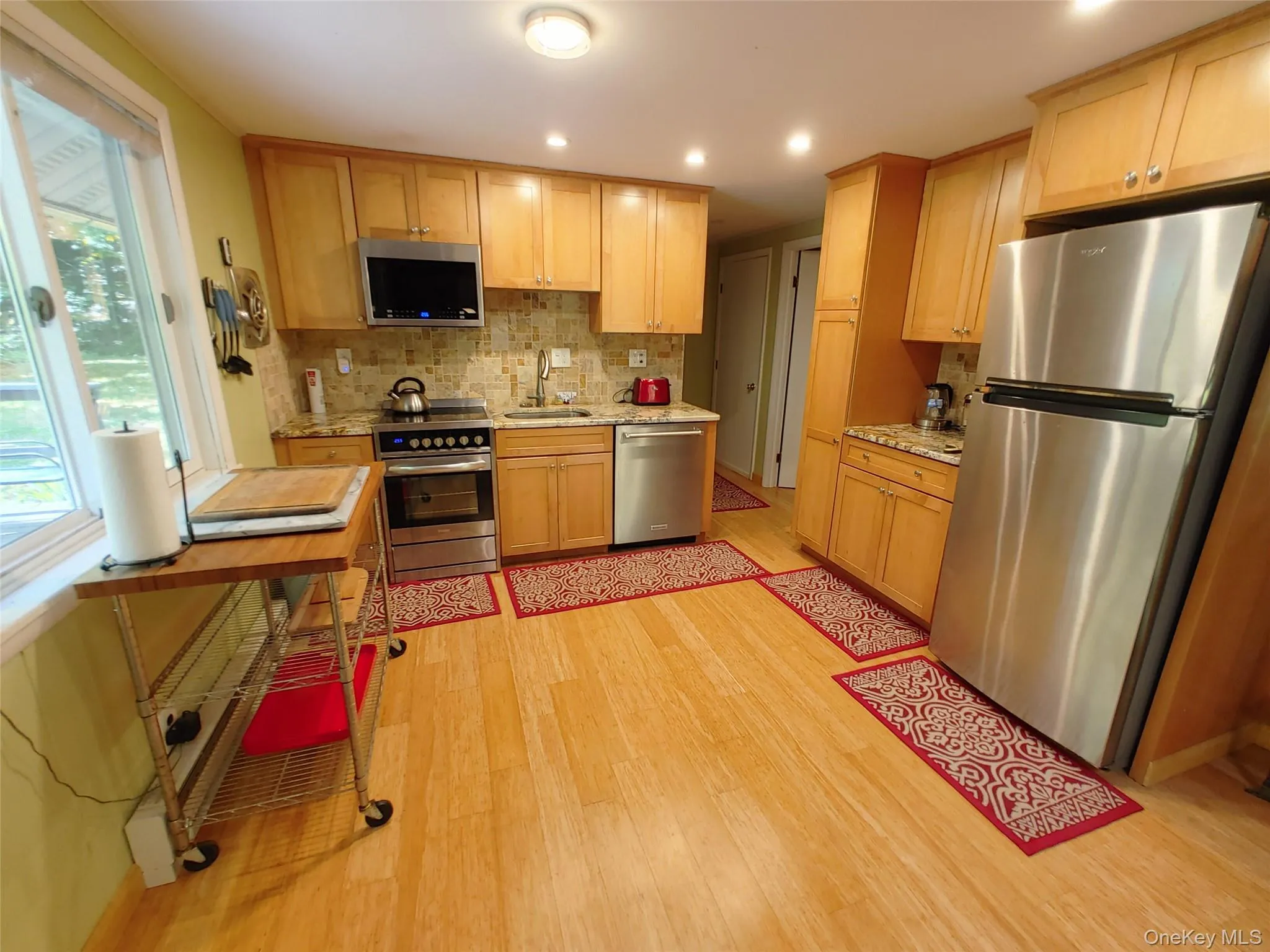 Kitchen with stainless steel appliances, bamboo plank floors, decorative backsplash, recessed lighting, and light brown maple wood cabinetry Kitchen with stainless steel appliances, bamboo plank floors, decorative backsplash, recessed lighting, and light brown maple wood cabinetry