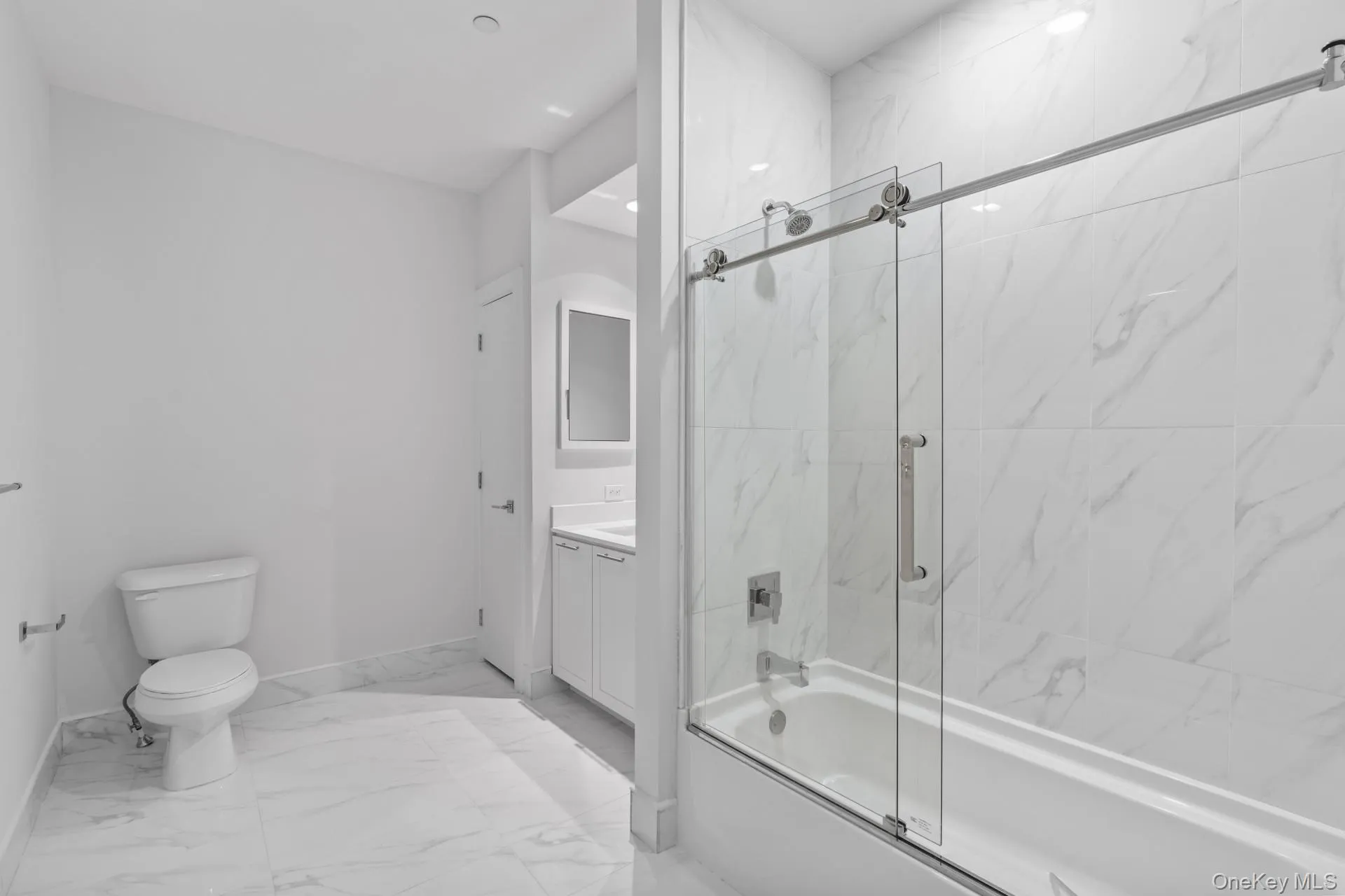 Bathroom with combined bath / shower with glass door, vanity, and marble look tiles Bathroom with combined bath / shower with glass door, vanity, and marble look tiles