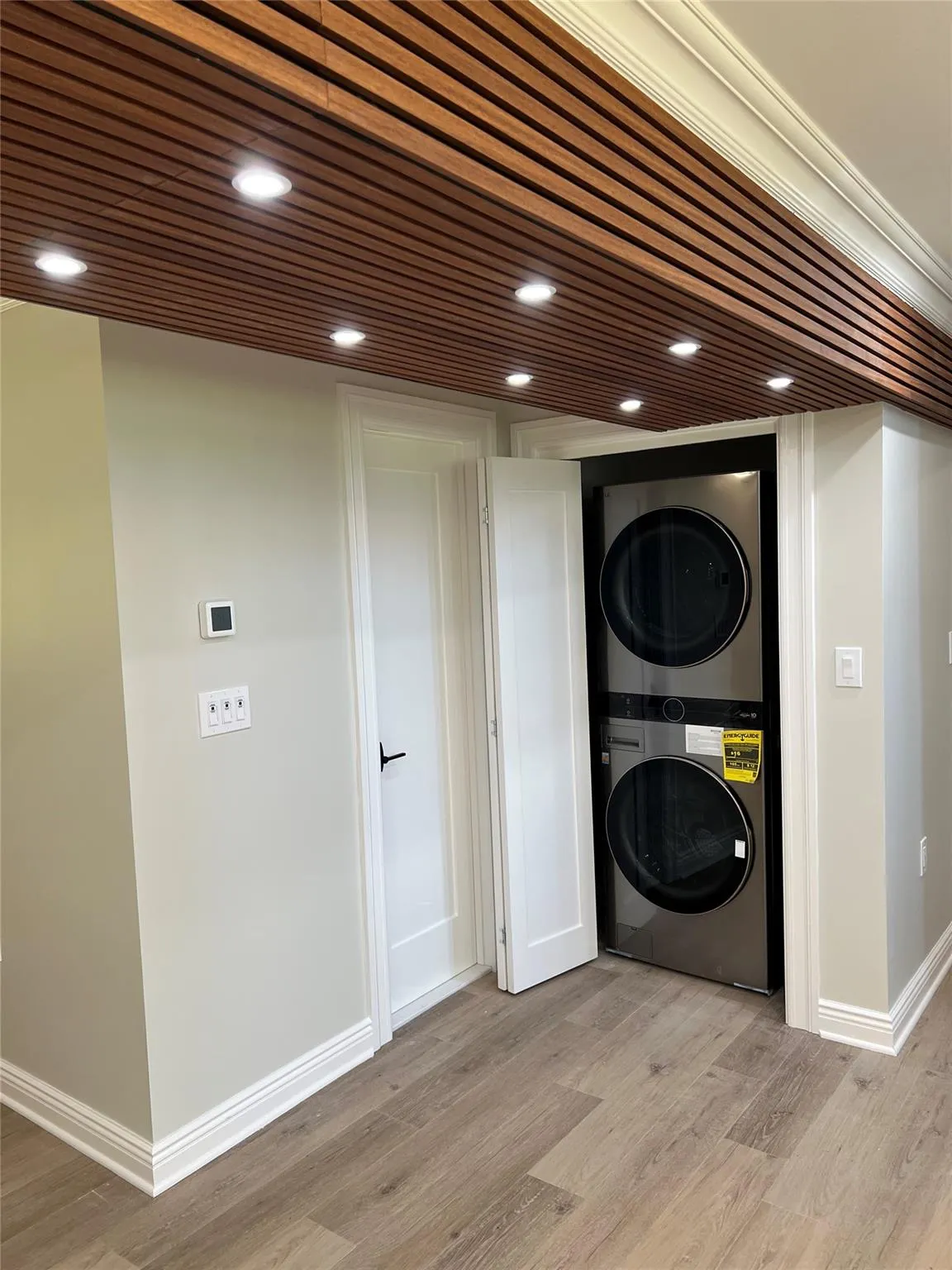 Washroom with stacked washer / dryer, light wood finished floors, and recessed lighting Washroom with stacked washer / dryer, light wood finished floors, and recessed lighting