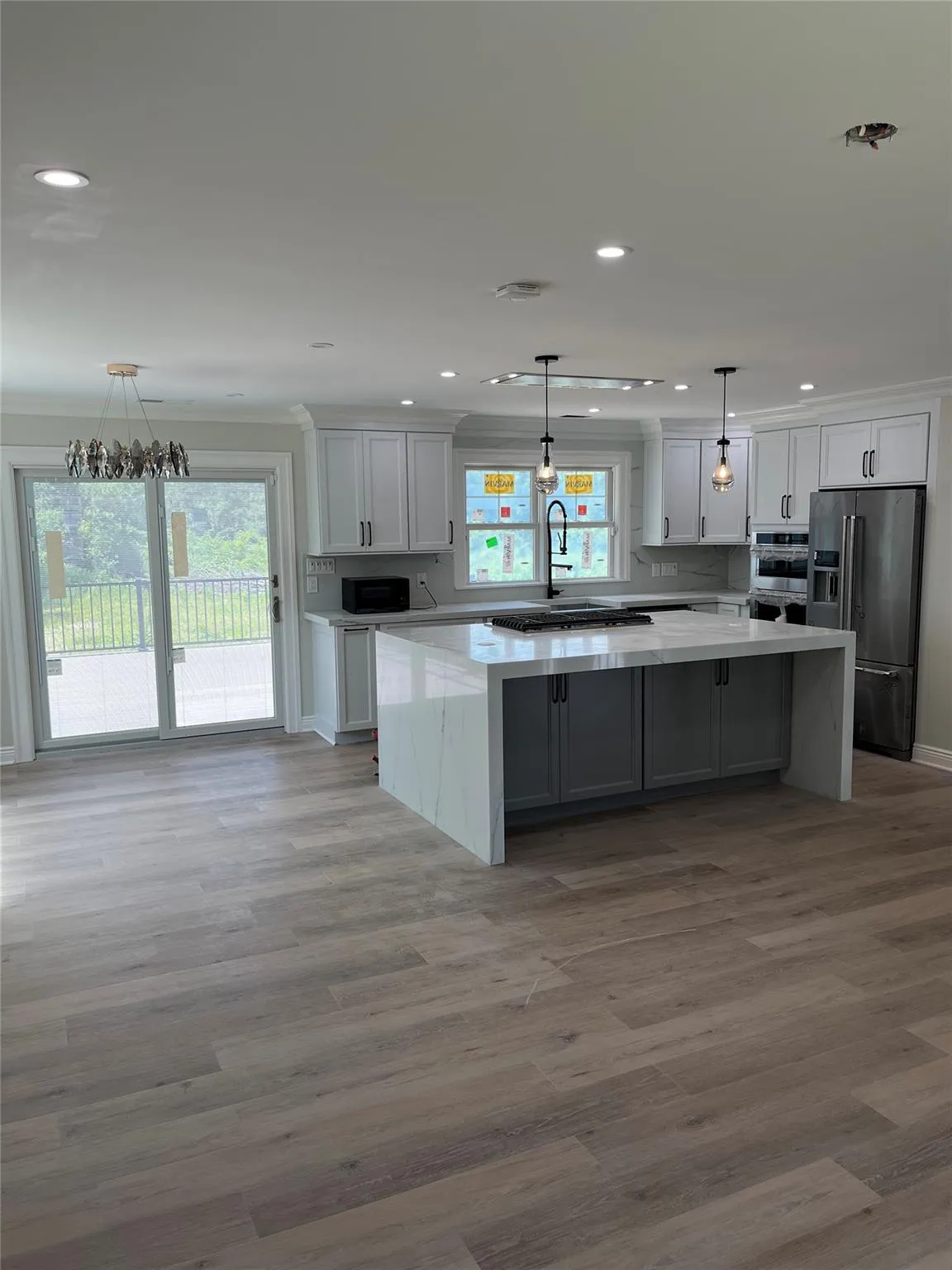 Kitchen featuring fridge with ice dispenser, a large island, healthy amount of natural light, crown molding, and wood finished floors Kitchen featuring fridge with ice dispenser, a large island, healthy amount of natural light, crown molding, and wood finished floors