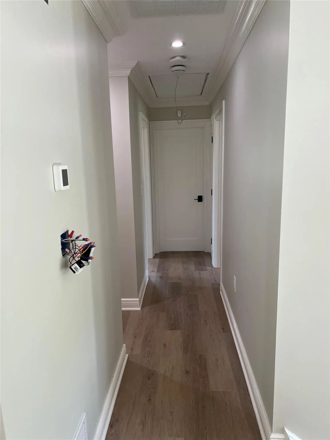 Hallway with attic access, ornamental molding, and wood finished floors Hallway with attic access, ornamental molding, and wood finished floors