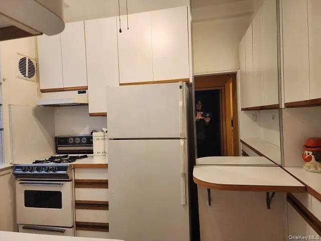 Kitchen with white appliances, under cabinet range hood, light countertops, and white cabinetry Kitchen with white appliances, under cabinet range hood, light countertops, and white cabinetry