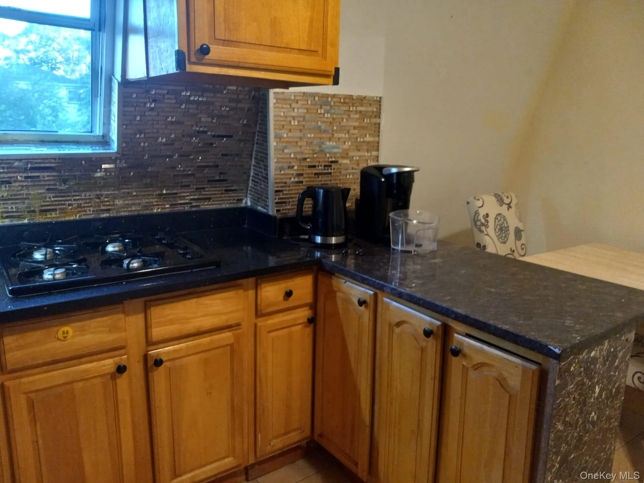 Kitchen featuring black gas cooktop, tasteful backsplash, dark stone countertops, and brown cabinets Kitchen featuring black gas cooktop, tasteful backsplash, dark stone countertops, and brown cabinets