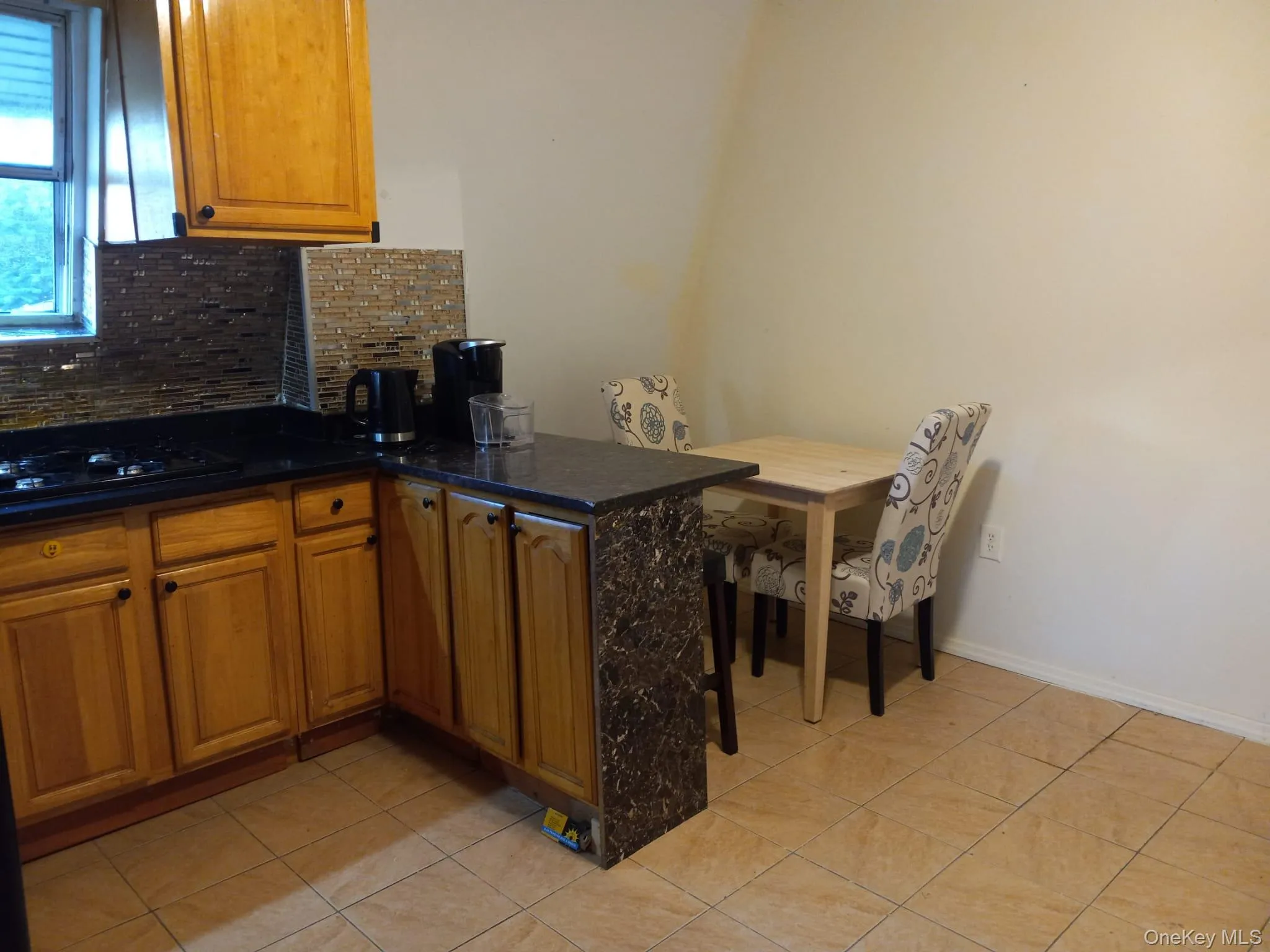 Kitchen with tasteful backsplash, black gas cooktop, light tile patterned floors, brown cabinetry, and a peninsula Kitchen with tasteful backsplash, black gas cooktop, light tile patterned floors, brown cabinetry, and a peninsula