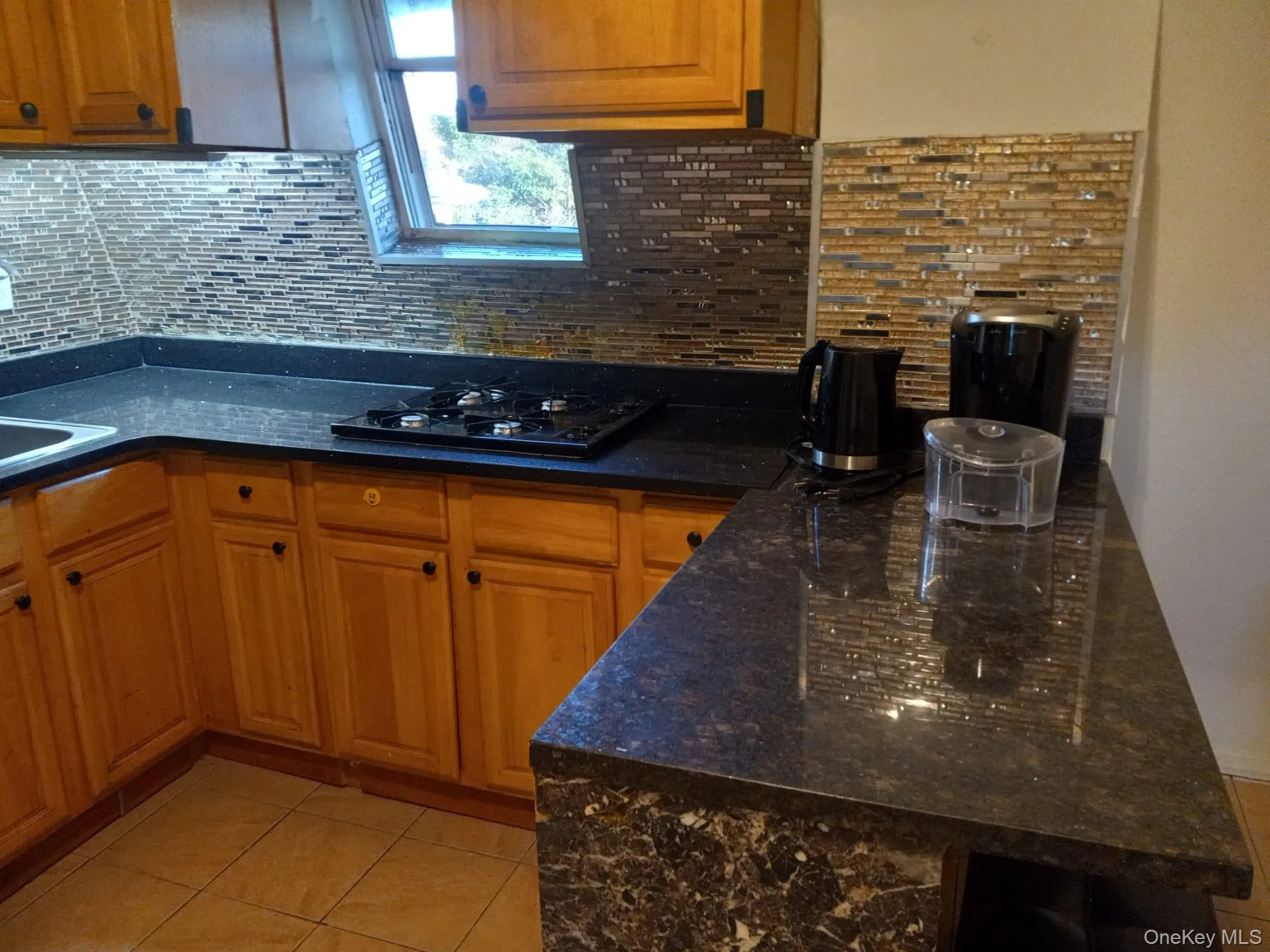 Kitchen featuring black gas cooktop, decorative backsplash, light tile patterned floors, and dark stone counters Kitchen featuring black gas cooktop, decorative backsplash, light tile patterned floors, and dark stone counters