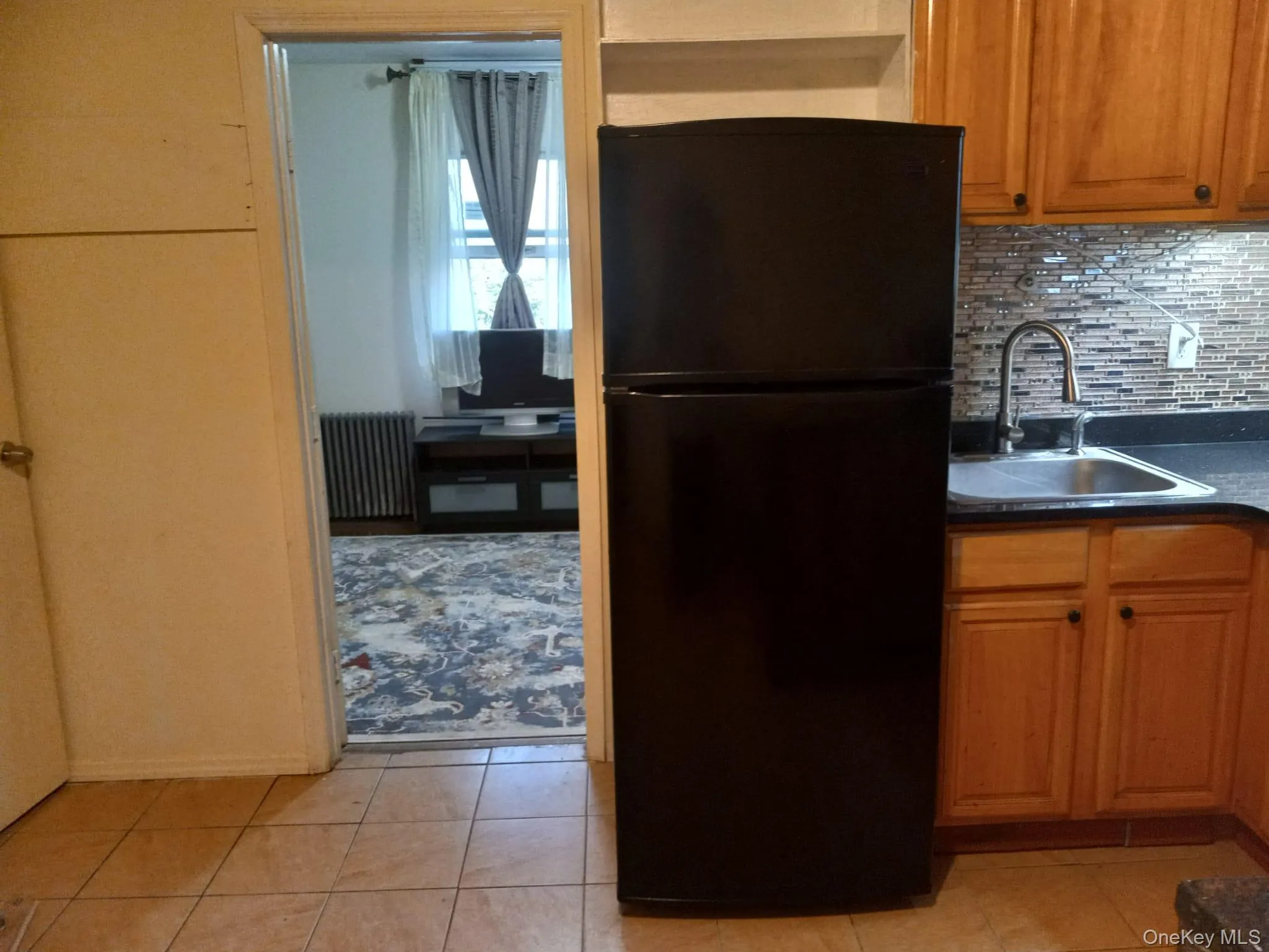 Kitchen featuring freestanding refrigerator, radiator, dark countertops, decorative backsplash, and light tile patterned floors Kitchen featuring freestanding refrigerator, radiator, dark countertops, decorative backsplash, and light tile patterned floors