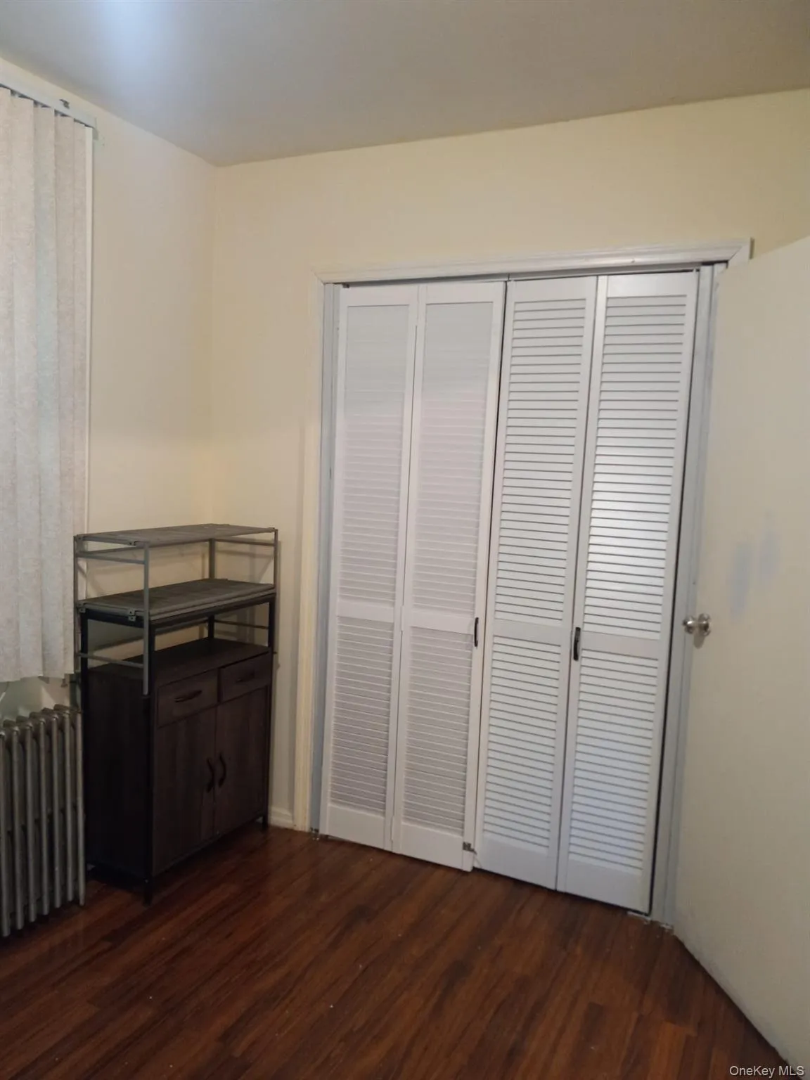 Unfurnished bedroom with radiator heating unit, dark wood-type flooring, and a closet Unfurnished bedroom with radiator heating unit, dark wood-type flooring, and a closet