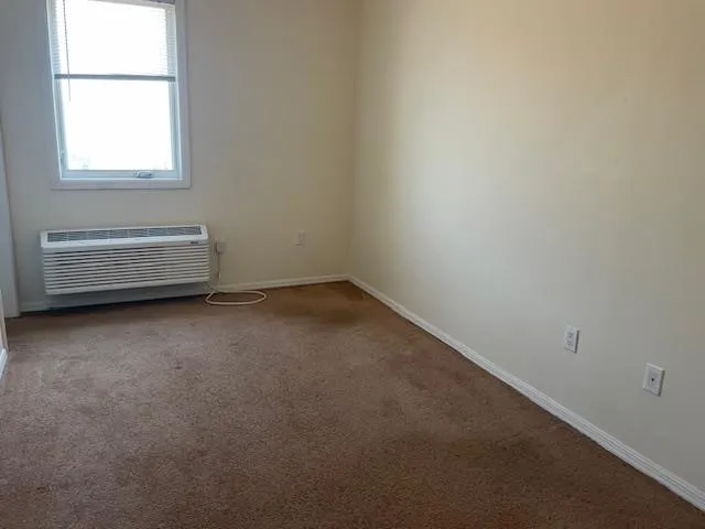 Empty room featuring carpet and a wall mounted AC Empty room featuring carpet and a wall mounted AC