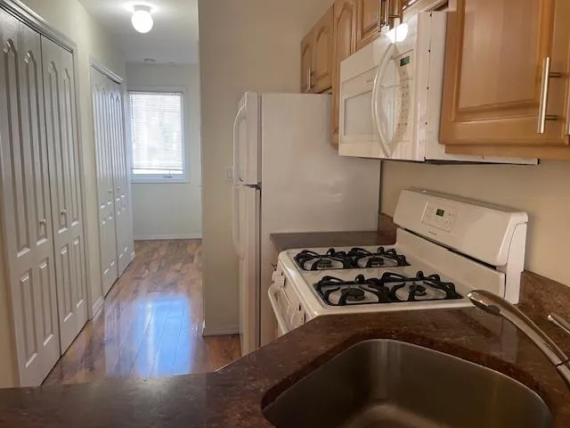 Kitchen featuring white appliances, wood finished floors, and dark stone counters Kitchen featuring white appliances, wood finished floors, and dark stone counters