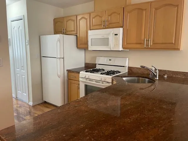 Kitchen with white appliances, dark stone counters, light wood-style floors, and light brown cabinetry Kitchen with white appliances, dark stone counters, light wood-style floors, and light brown cabinetry