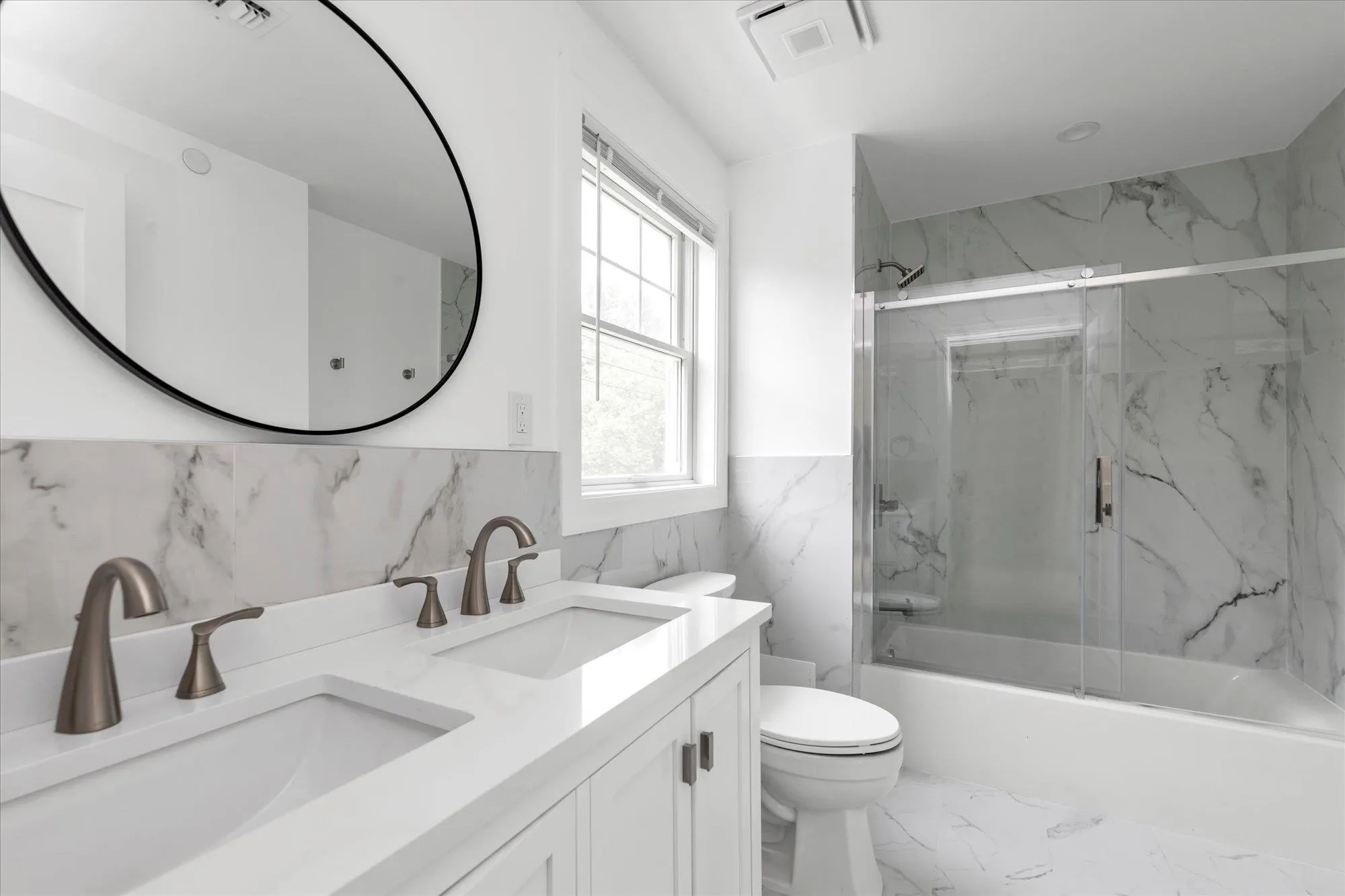 Bathroom featuring double vanity, enclosed tub / shower combo, wainscoting, marble finish floors, and tile walls Bathroom featuring double vanity, enclosed tub / shower combo, wainscoting, marble finish floors, and tile walls