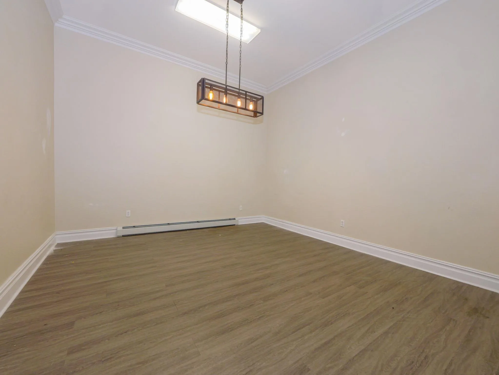 Unfurnished room with baseboard heating, ornamental molding, wood finished floors, and a chandelier Unfurnished room with baseboard heating, ornamental molding, wood finished floors, and a chandelier