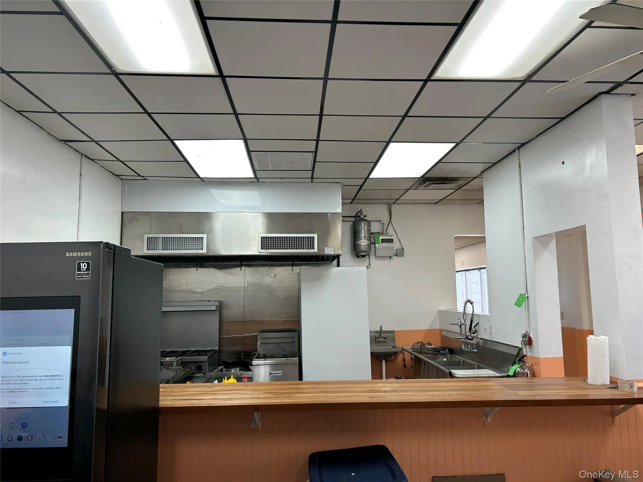 Kitchen with freestanding refrigerator, butcher block countertops, and a drop ceiling Kitchen with freestanding refrigerator, butcher block countertops, and a drop ceiling