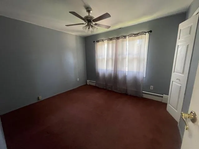 Bedroom with dark colored carpet, ceiling fan, and a baseboard heating unit Bedroom with dark colored carpet, ceiling fan, and a baseboard heating unit
