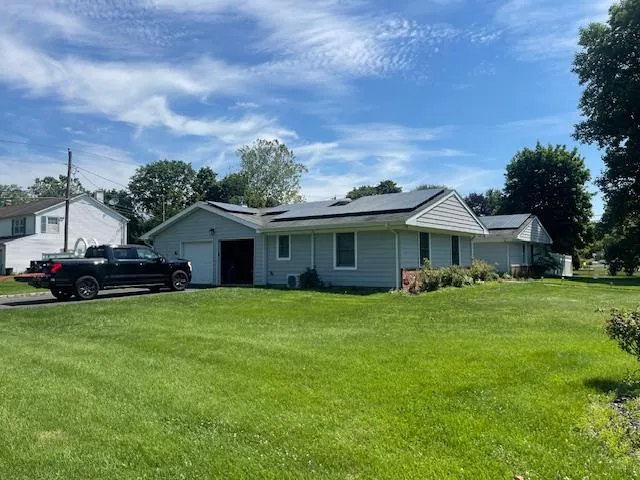 Ranch-style home featuring an attached garage, solar panels, and a front yard Ranch-style home featuring an attached garage, solar panels, and a front yard