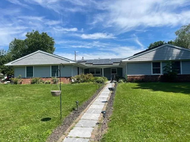 Ranch-style home with brick siding, roof mounted solar panels, and a front yard Ranch-style home with brick siding, roof mounted solar panels, and a front yard