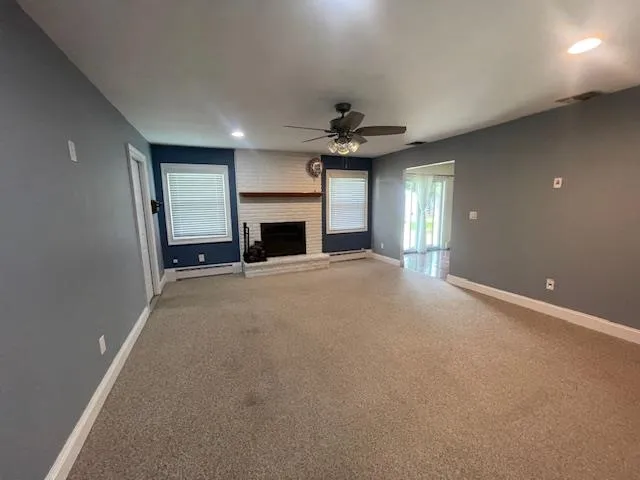 Unfurnished living room featuring baseboard heating, ceiling fan, light carpet, healthy amount of natural light, and recessed lighting Unfurnished living room featuring baseboard heating, ceiling fan, light carpet, healthy amount of natural light, and recessed lighting