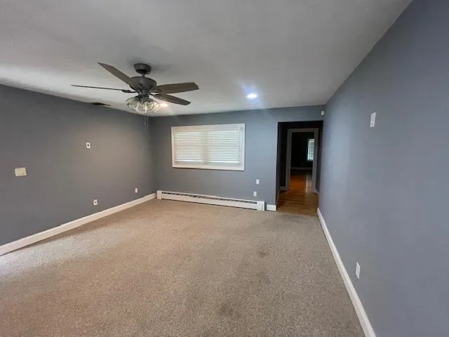Empty room with a baseboard radiator, a ceiling fan, carpet floors, and recessed lighting Empty room with a baseboard radiator, a ceiling fan, carpet floors, and recessed lighting