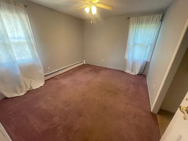 Bedroom featuring a baseboard heating unit, healthy amount of natural light, carpet flooring, and ceiling fan Bedroom featuring a baseboard heating unit, healthy amount of natural light, carpet flooring, and ceiling fan