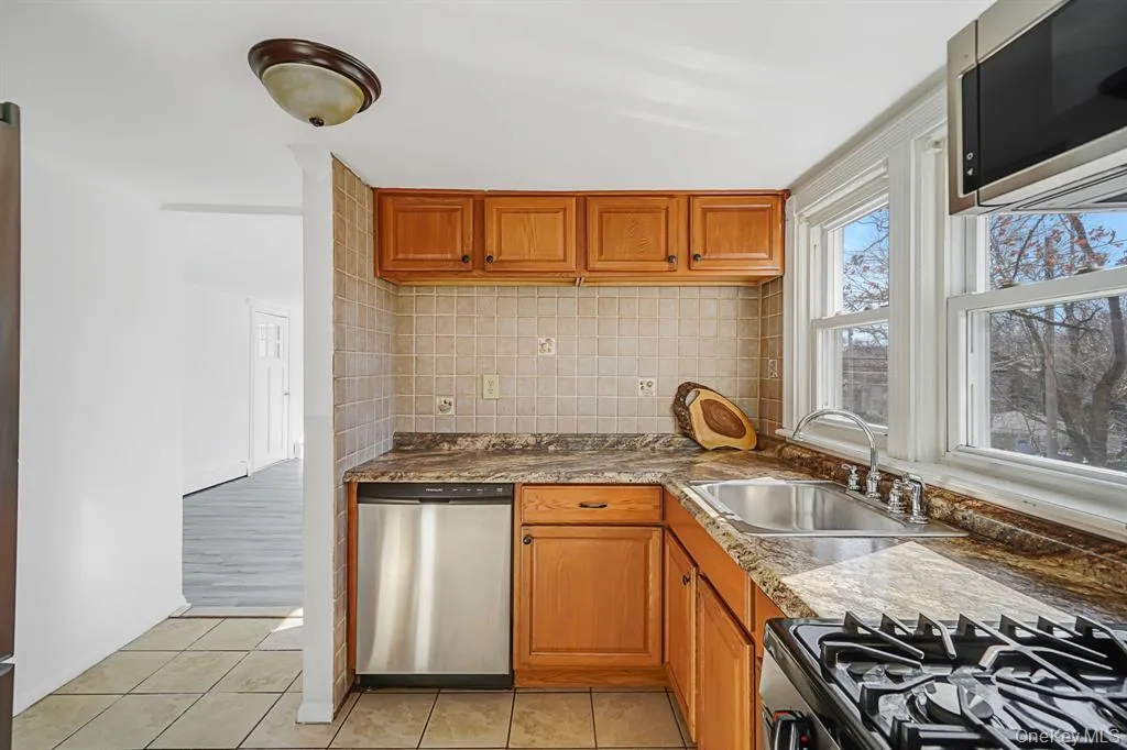 Kitchen featuring stainless steel appliances, light tile patterned floors, decorative backsplash, and brown cabinets Kitchen featuring stainless steel appliances, light tile patterned floors, decorative backsplash, and brown cabinets
