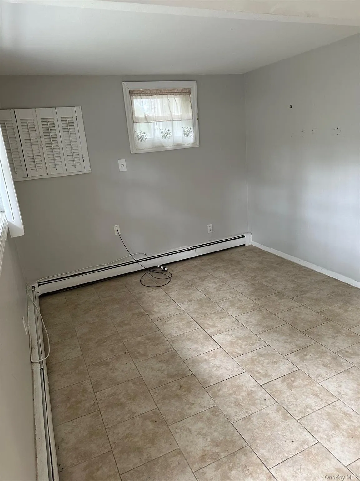 Empty room featuring light tile patterned flooring and baseboard heating Empty room featuring light tile patterned flooring and baseboard heating