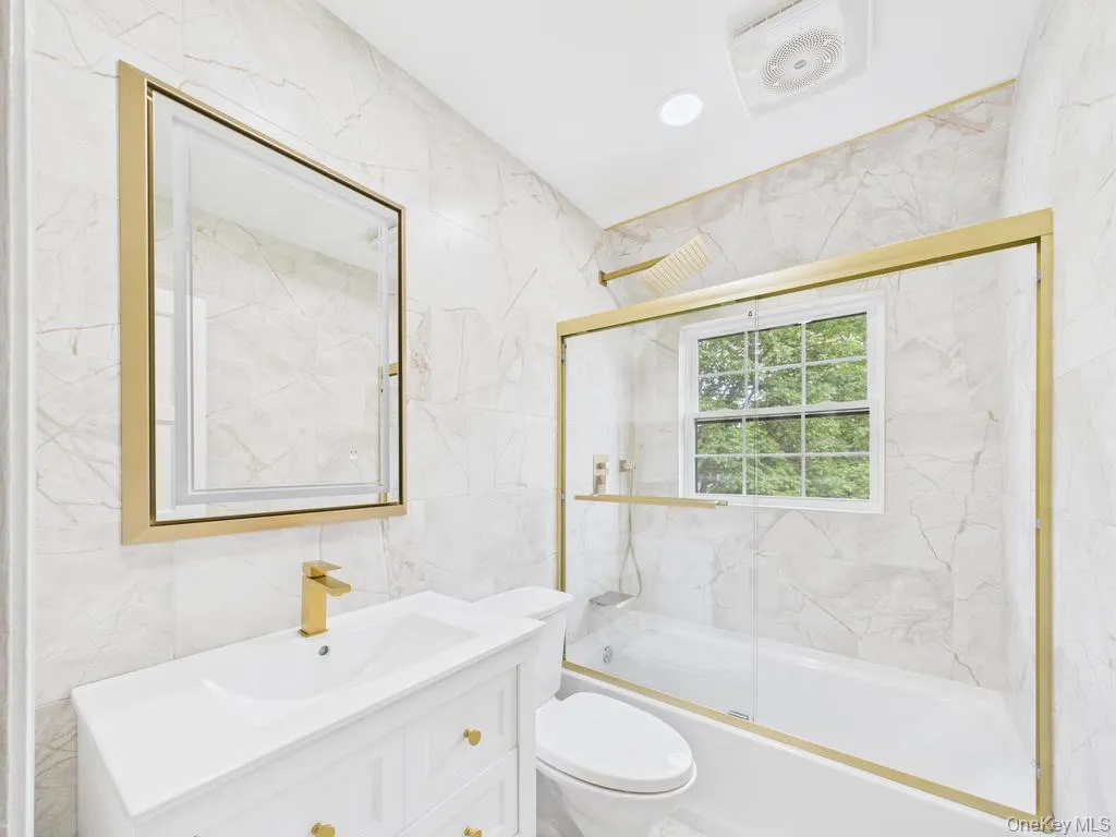 Bathroom featuring tile walls, vanity, and bath / shower combo with glass door Bathroom featuring tile walls, vanity, and bath / shower combo with glass door