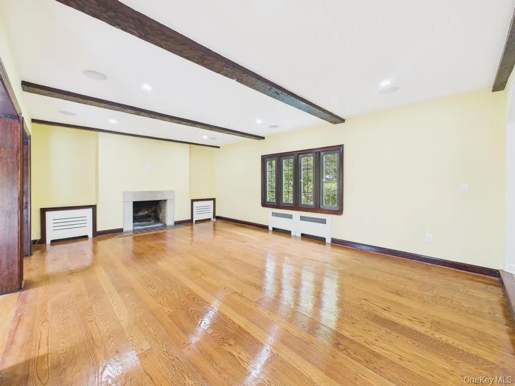 Unfurnished living room with a fireplace with flush hearth, beam ceiling, light wood-style flooring, recessed lighting, and radiator Unfurnished living room with a fireplace with flush hearth, beam ceiling, light wood-style flooring, recessed lighting, and radiator