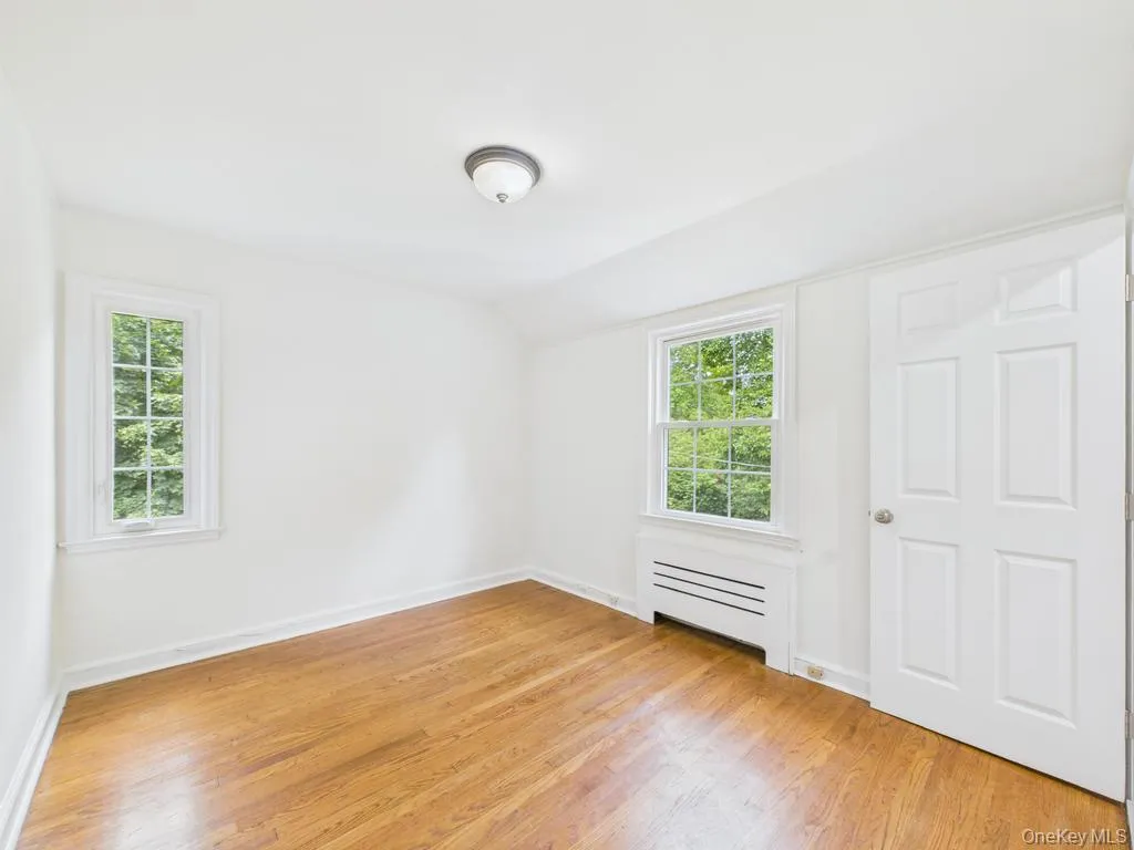 Empty room featuring light wood-type flooring, lofted ceiling, healthy amount of natural light, and radiator Empty room featuring light wood-type flooring, lofted ceiling, healthy amount of natural light, and radiator