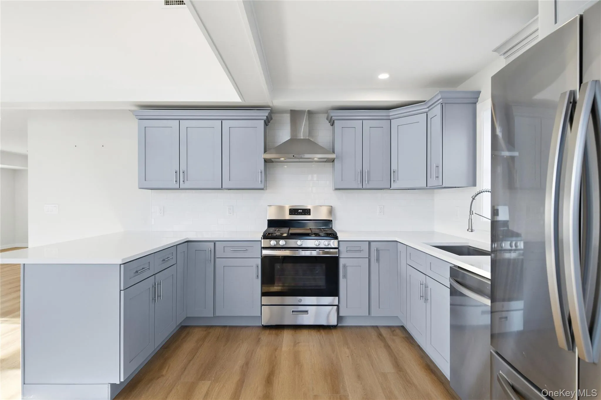 Kitchen featuring stainless steel appliances, decorative backsplash, wall chimney exhaust hood, gray cabinetry, and a peninsula Kitchen featuring stainless steel appliances, decorative backsplash, wall chimney exhaust hood, gray cabinetry, and a peninsula