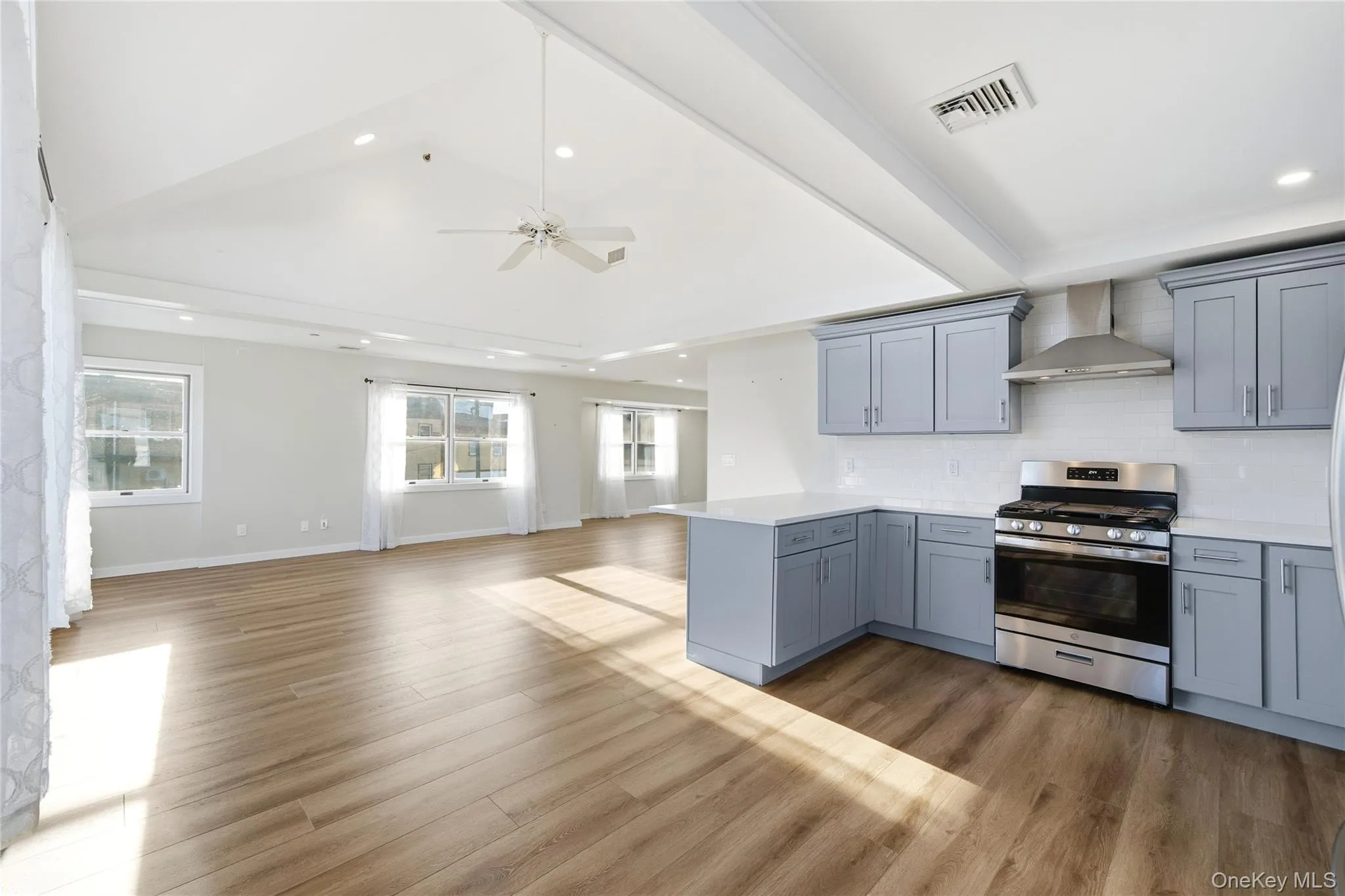 Kitchen featuring gas range, gray cabinets, decorative backsplash, wall chimney exhaust hood, and light wood-type flooring Kitchen featuring gas range, gray cabinets, decorative backsplash, wall chimney exhaust hood, and light wood-type flooring