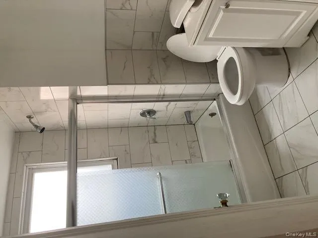 Full bath featuring bath / shower combo with glass door, marble finish flooring, and tile walls Full bath featuring bath / shower combo with glass door, marble finish flooring, and tile walls