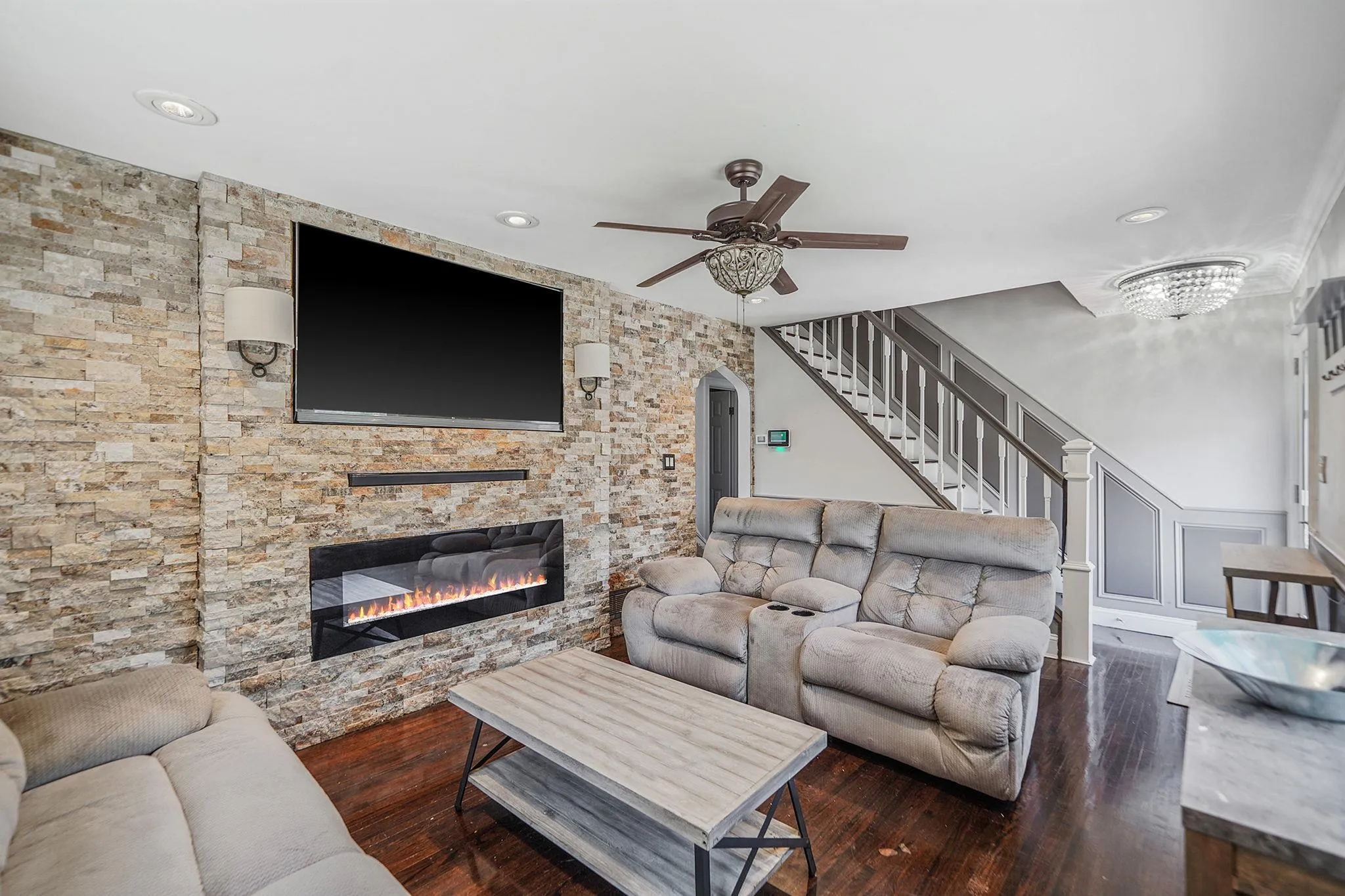 Living area with a fireplace, ceiling fan, arched walkways, hardwood / wood-style floors, and stairs Living area with a fireplace, ceiling fan, arched walkways, hardwood / wood-style floors, and stairs