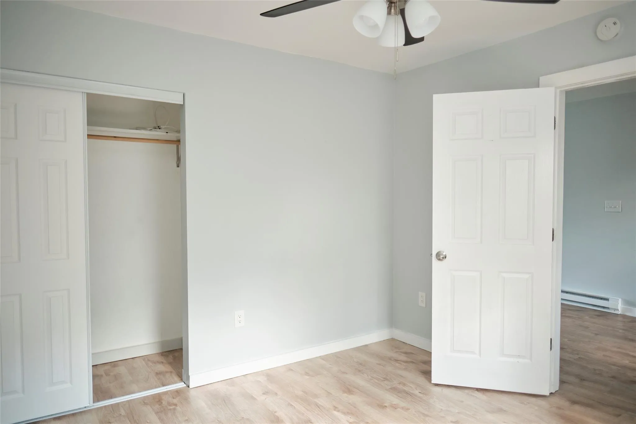 Unfurnished bedroom featuring a baseboard heating unit, light wood finished floors, a closet, and a ceiling fan Unfurnished bedroom featuring a baseboard heating unit, light wood finished floors, a closet, and a ceiling fan