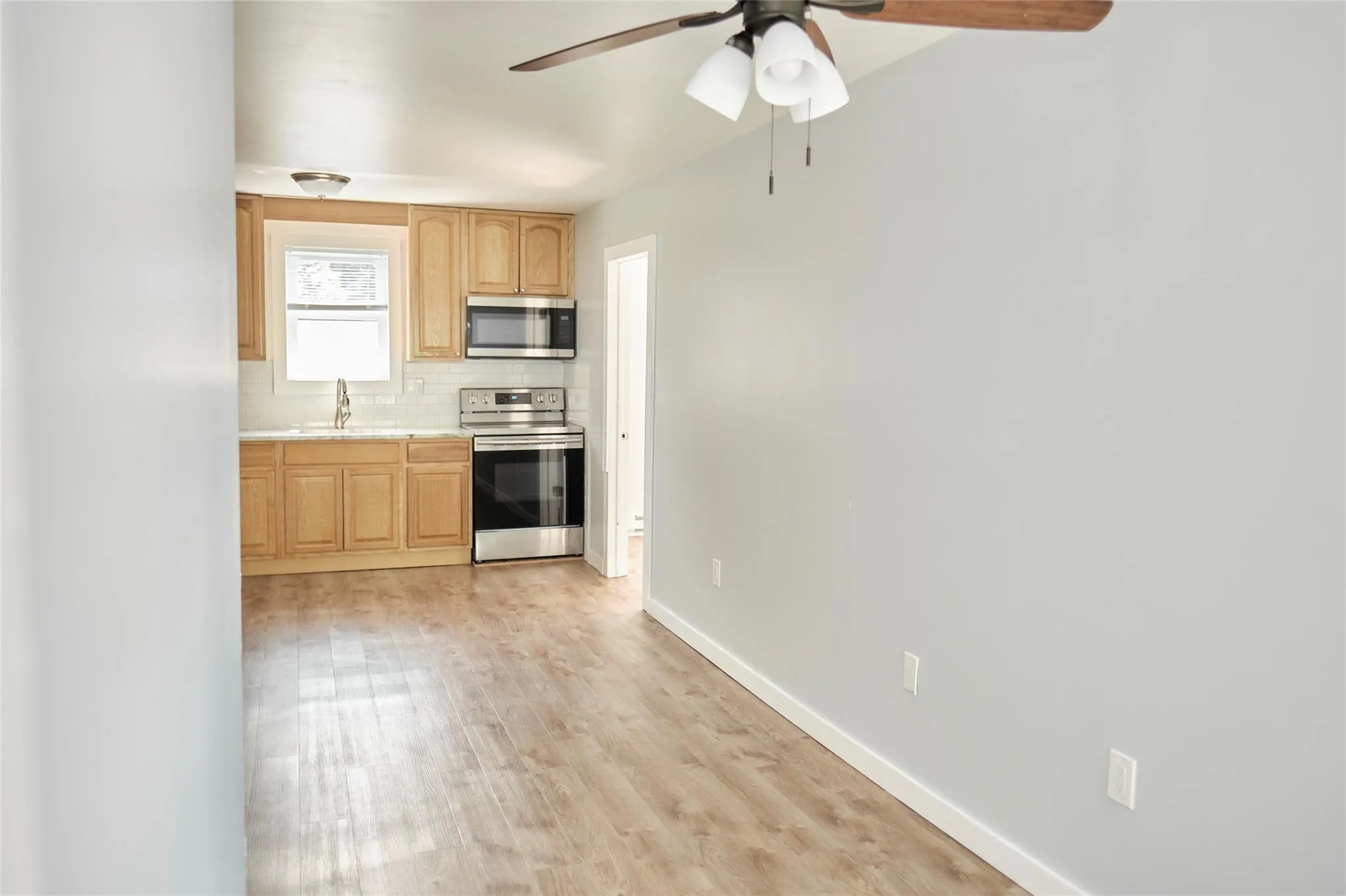 Kitchen with appliances with stainless steel finishes, a ceiling fan, decorative backsplash, light countertops, and light wood-style floors Kitchen with appliances with stainless steel finishes, a ceiling fan, decorative backsplash, light countertops, and light wood-style floors