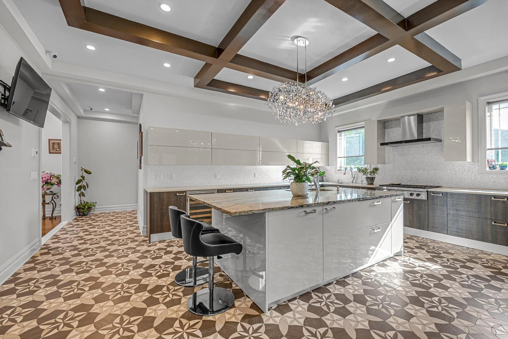 Kitchen with wall chimney range hood, modern cabinets, coffered ceiling, a large island, and healthy amount of natural light Kitchen with wall chimney range hood, modern cabinets, coffered ceiling, a large island, and healthy amount of natural light