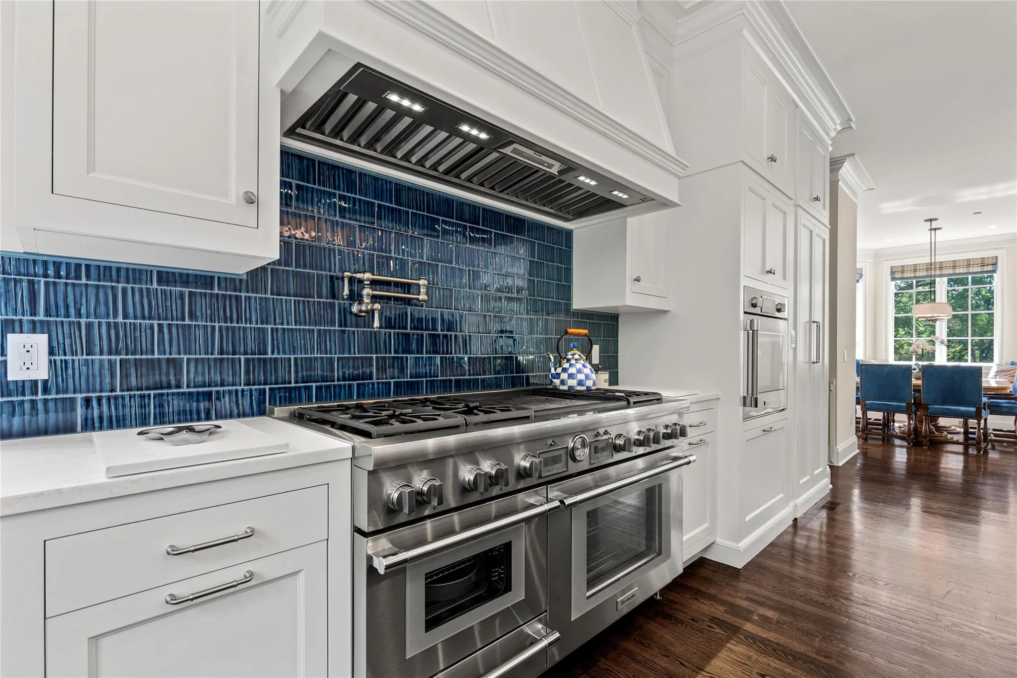 Kitchen with appliances with stainless steel finishes, custom range hood, backsplash, dark wood-style floors, and white cabinets Kitchen with appliances with stainless steel finishes, custom range hood, backsplash, dark wood-style floors, and white cabinets