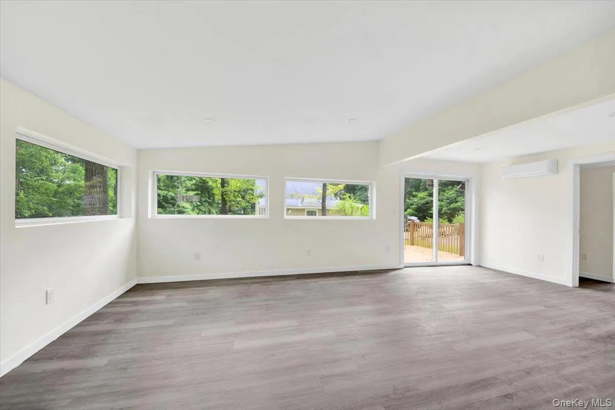 Unfurnished room featuring a wall mounted AC, healthy amount of natural light, wood finished floors, and vaulted ceiling Unfurnished room featuring a wall mounted AC, healthy amount of natural light, wood finished floors, and vaulted ceiling