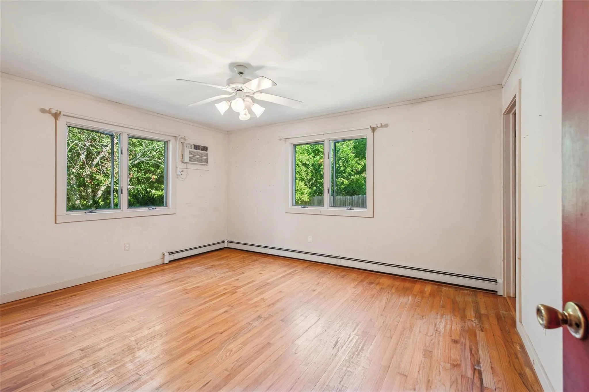 Empty room with healthy amount of natural light, a baseboard radiator, hardwood / wood-style floors, a wall unit AC, and crown molding Empty room with healthy amount of natural light, a baseboard radiator, hardwood / wood-style floors, a wall unit AC, and crown molding
