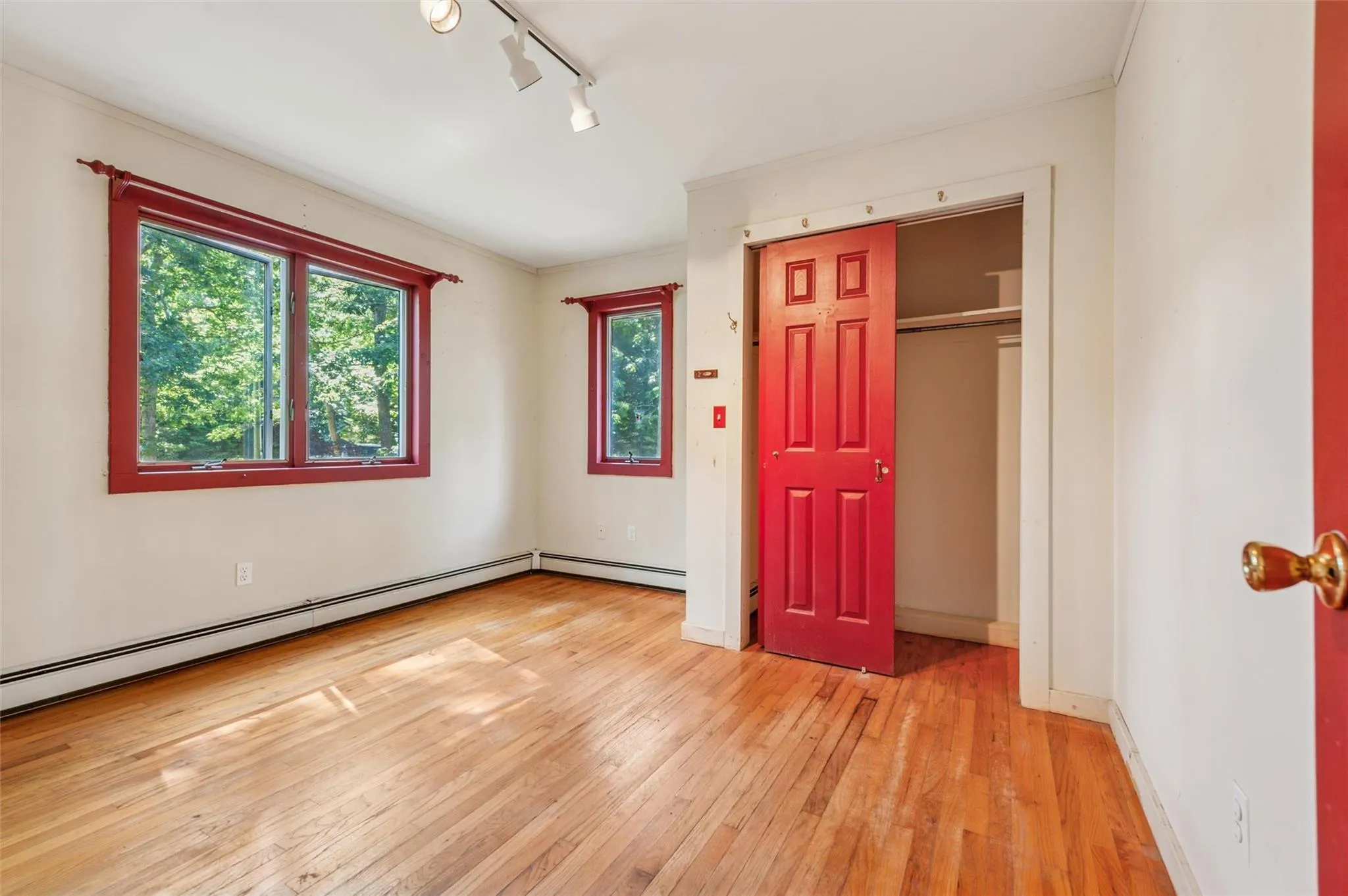 Unfurnished bedroom featuring light wood-type flooring, baseboard heating, rail lighting, a closet, and crown molding Unfurnished bedroom featuring light wood-type flooring, baseboard heating, rail lighting, a closet, and crown molding