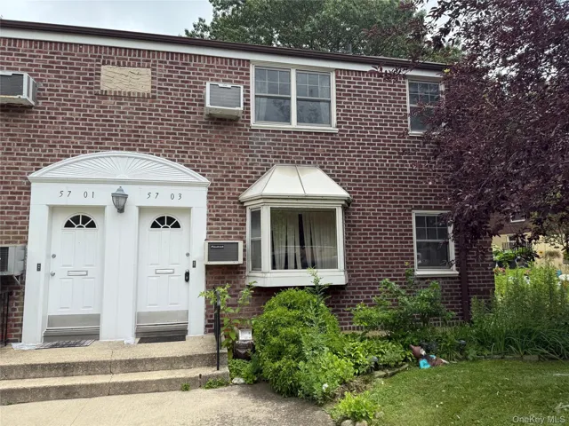 View of front facade with brick siding and a wall mounted air conditioner