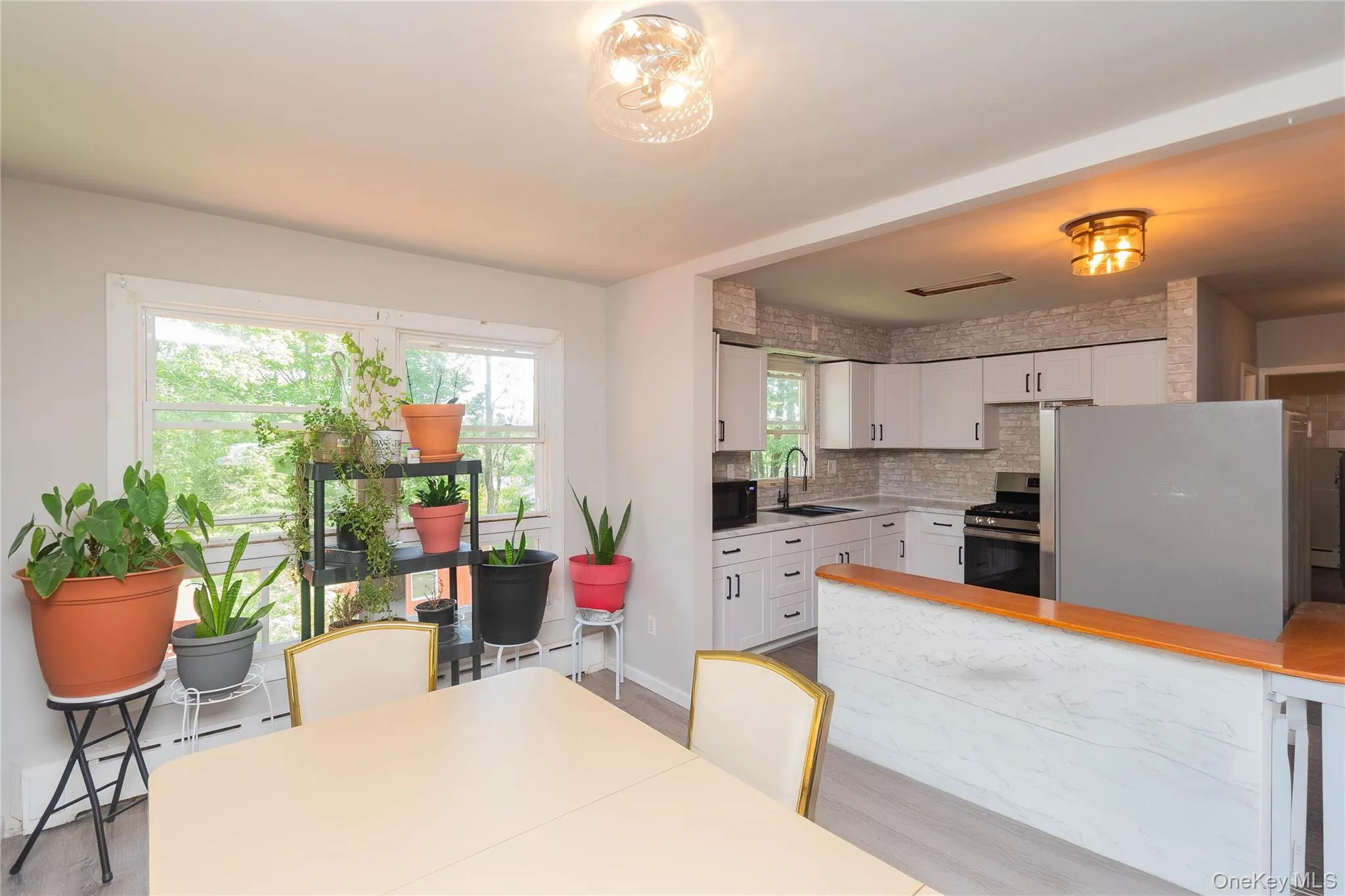 Kitchen featuring stainless steel appliances, white cabinets, light wood-style flooring, and tasteful backsplash Kitchen featuring stainless steel appliances, white cabinets, light wood-style flooring, and tasteful backsplash