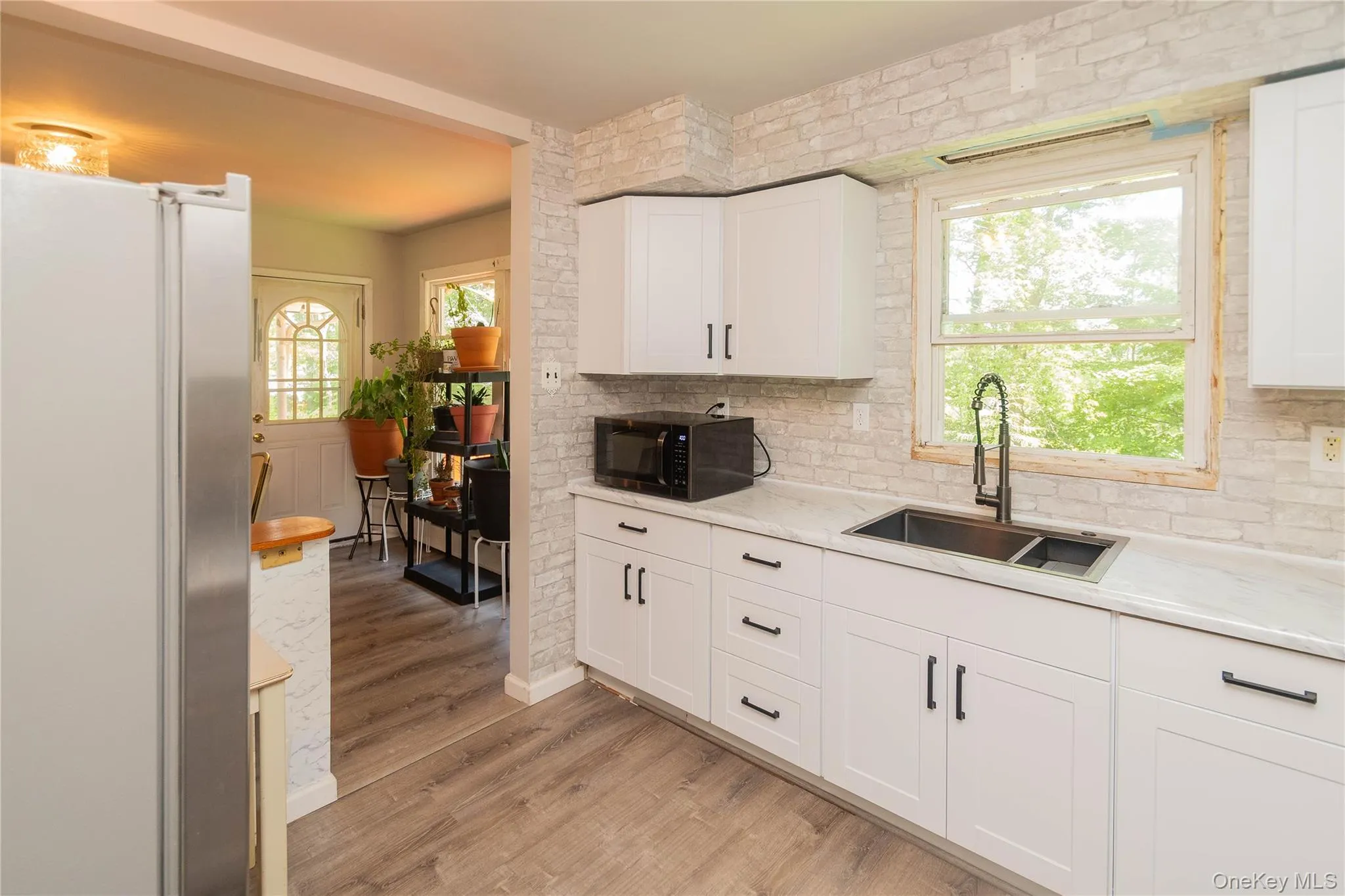 Kitchen with black microwave, freestanding refrigerator, plenty of natural light, and light wood finished floors Kitchen with black microwave, freestanding refrigerator, plenty of natural light, and light wood finished floors