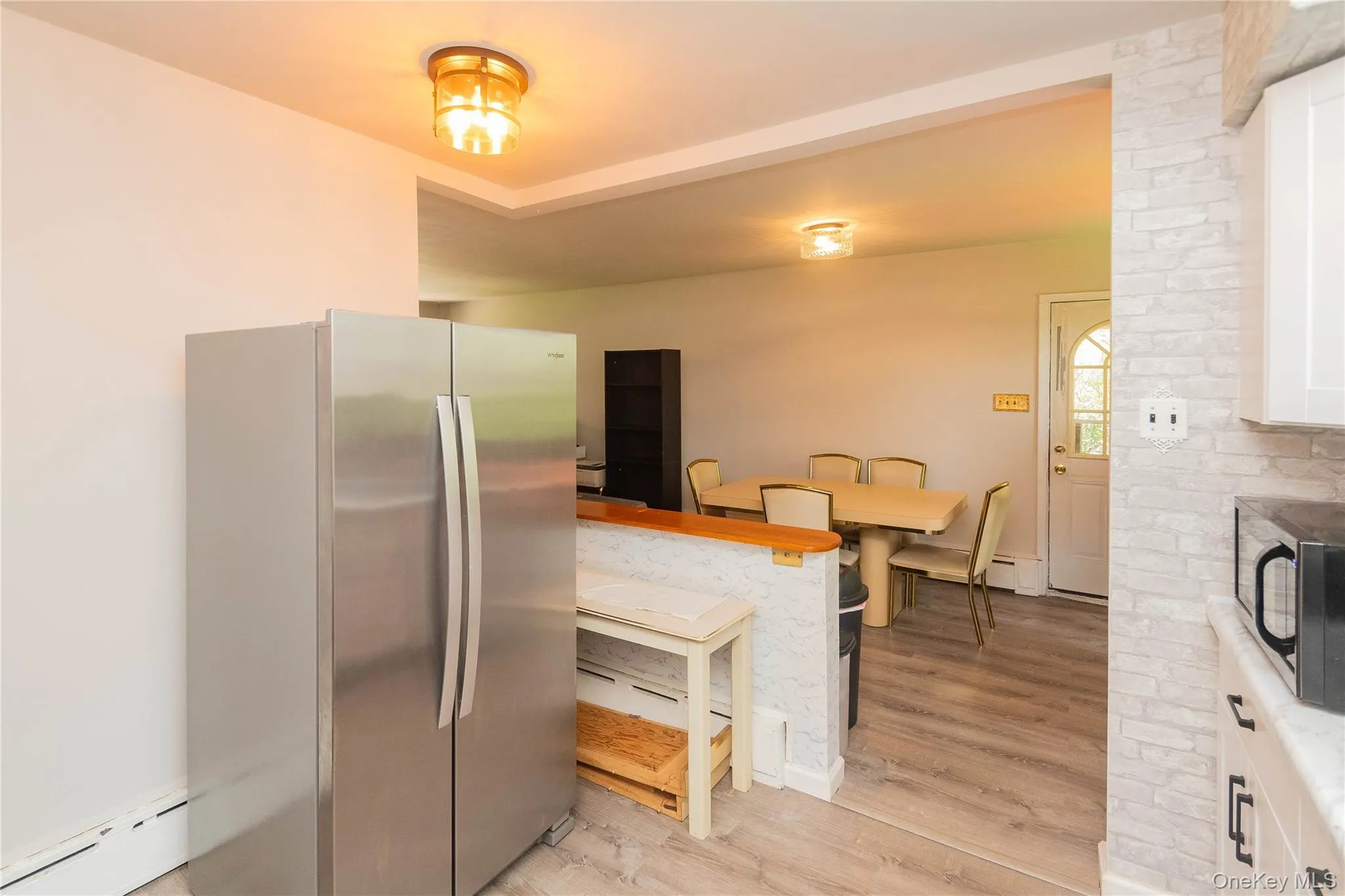 Kitchen featuring stainless steel appliances, a baseboard radiator, white cabinetry, light wood-style flooring, and a breakfast bar area Kitchen featuring stainless steel appliances, a baseboard radiator, white cabinetry, light wood-style flooring, and a breakfast bar area