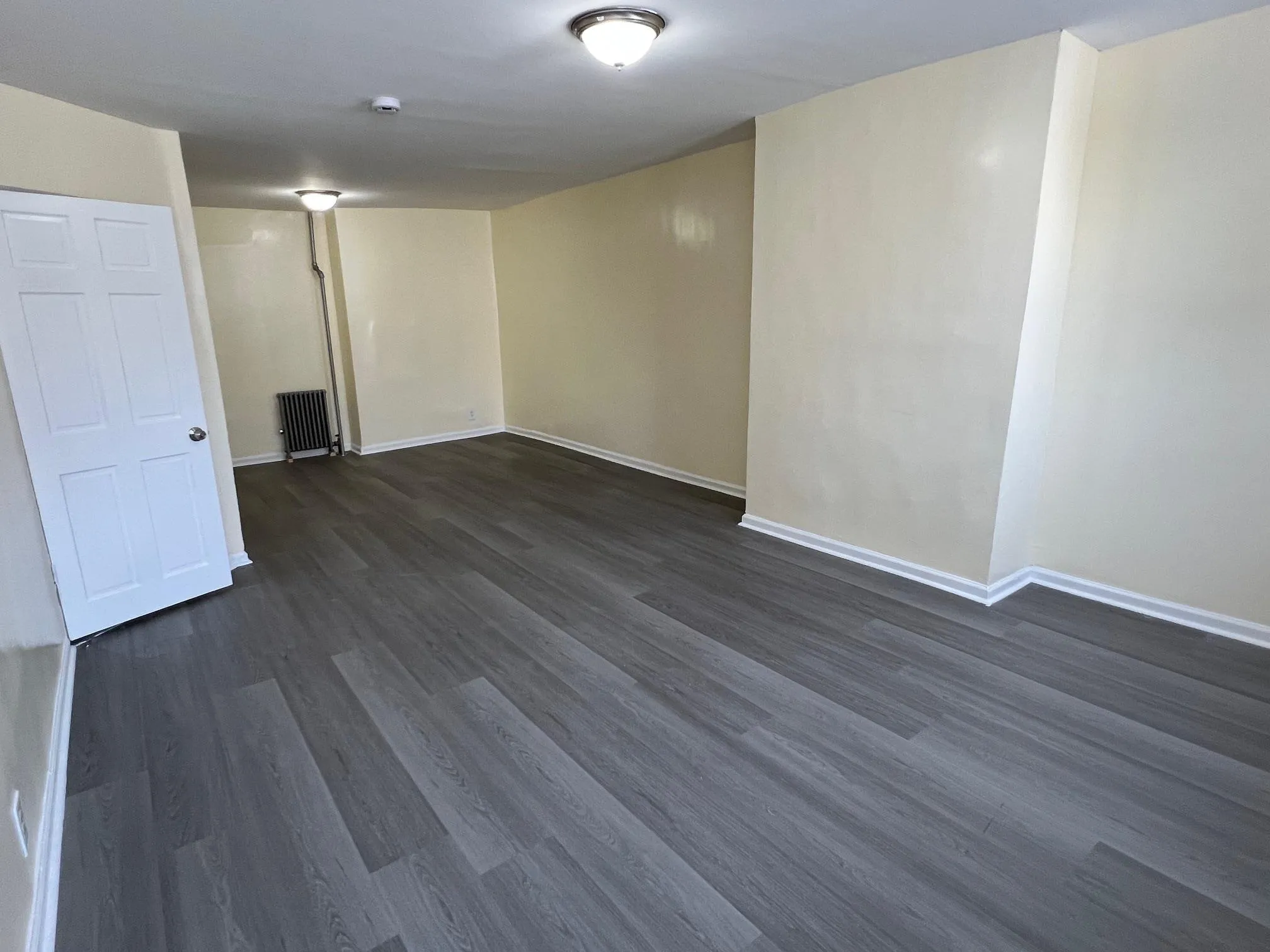 Empty room featuring dark wood finished floors, radiator heating unit, and a smoke detector Empty room featuring dark wood finished floors, radiator heating unit, and a smoke detector