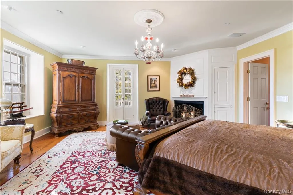 Bedroom with crown molding, a chandelier, wood finished floors, and a lit fireplace Bedroom with crown molding, a chandelier, wood finished floors, and a lit fireplace
