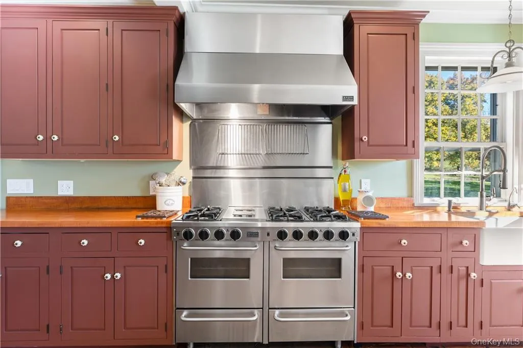 Kitchen with range with two ovens, wall chimney exhaust hood, wooden counters, and decorative light fixtures Kitchen with range with two ovens, wall chimney exhaust hood, wooden counters, and decorative light fixtures