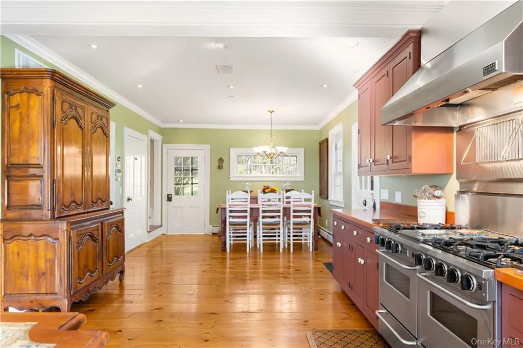 Kitchen with wall chimney exhaust hood, a chandelier, light wood finished floors, pendant lighting, and crown molding Kitchen with wall chimney exhaust hood, a chandelier, light wood finished floors, pendant lighting, and crown molding