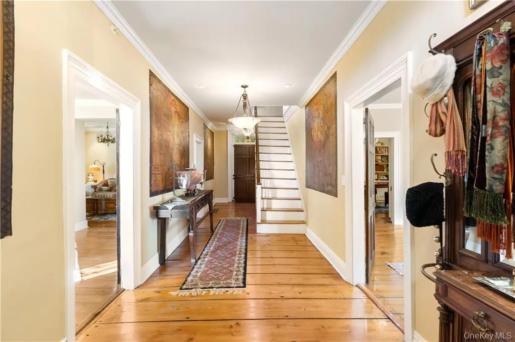 Corridor featuring light wood-style flooring, ornamental molding, and stairs Corridor featuring light wood-style flooring, ornamental molding, and stairs
