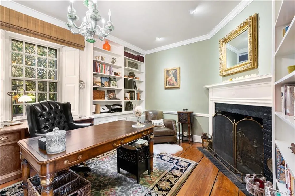 Office space featuring light wood-style flooring, crown molding, a fireplace with flush hearth, and a chandelier Office space featuring light wood-style flooring, crown molding, a fireplace with flush hearth, and a chandelier
